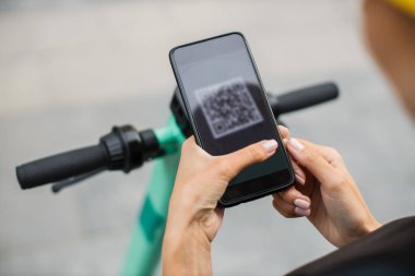 Kadın, sokakta elektrikli scooter 'ı açmak ve kiralamak için akıllı telefonla QR kodunu tarıyor.