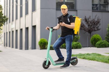 Sırt çantalı yiyecek teslimatçısı cep telefonunu bekliyor.