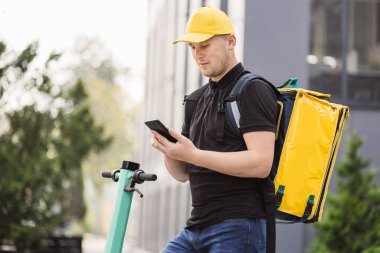 Kurye bir restorandan yemek teslimatı yapmak için cep telefonuna bakıyor..