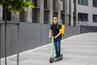 Şehirdeki caddelerde scooter kullanan bir erkek kurye. Paket ve restoranlardan eve sıcak yemek getiriyor.
