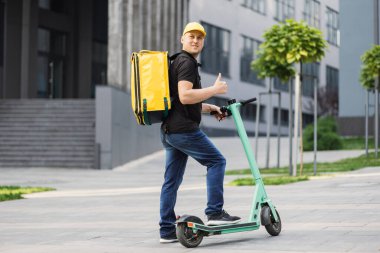 Sarı termal çantalı, elektrikli scooter kullanan mutlu genç teslimatçı.