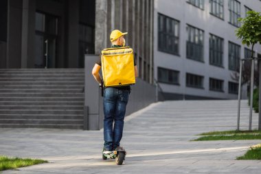 İzotermal yiyecek kutusuyla motosikletli, sarısı maskeli paket servis elemanı..