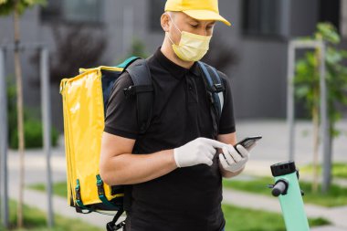 Adresi iletmek için cep telefonuna bakan yüz maskeli kuryeyi kapat.