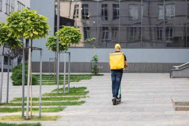 Yüz maskeli kuryenin trafik sıkışıklığından kaçınmak için scooter kullanarak yiyecek dağıtırken görüntüsü.