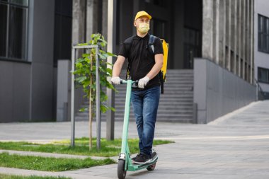 Sarı maskeli ve termal sırt çantalı kurye yemek teslimatı.