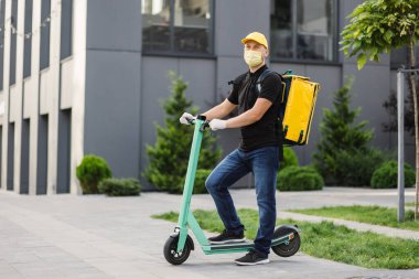 Kurye, sarı yüz koruyucu maske takarak elektrikli scooterla yemek getiriyor.
