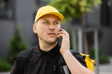 Sırt çantalı sarı şapkalı teslimatçının portresi akıllı telefon kullanarak siparişleri kontrol ediyor.