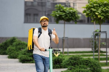 Yemek teslimatı için arkada sarı sırt çantası olan elektrikli scooter şoförü yemek teslimatı için yola çıktı.