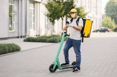 Elektrikli scooterlı izotermal yiyecek kutusu olan erkek kurye eve gelir ve müşteri çağırır.
