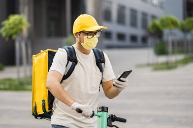 Adresi iletmek için cep telefonuna bakan yüz maskeli kuryeyi kapat.