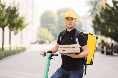 Pizza yiyen erkek kurye kameraya bakıyor.