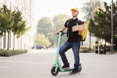 Şehrin sokaklarında scooter kullanan kurye pizza kutusundan paket servis ediliyor..