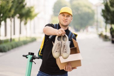 Kurye kameraya bakarak kutuyu açar ve spor ayakkabılarını çıkarır..