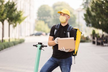Yakışıklı genç adam, elektronik scooter kullanıyor. İnternetteki bir karton kutunun içinde malları teslim etmek için.