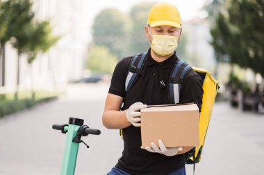Koruyucu yüz maskesi takmış, Scooter 'da karton kutusu olan bir kurye.,