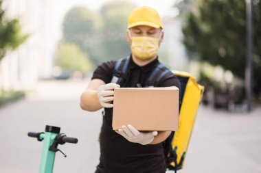 Koruyucu yüz maskesi takmış, Scooter 'da karton kutusu olan bir kurye.,