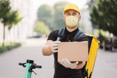 Koruyucu yüz maskesi takmış, Scooter 'da karton kutusu olan bir kurye.,