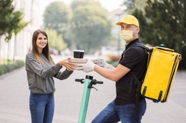 Çekici genç teslimatçı elinde sıcak pizza ve iki fincan sıcak kahve olan kutular tutuyor..