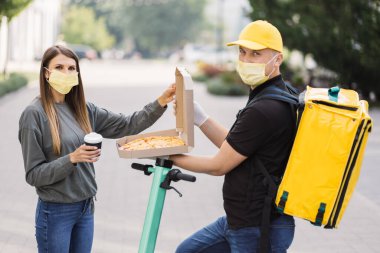 Pizza teslimatı. Sarı üniformalı ve yüz maskeli kurye kadınlara yemek siparişi veriyor..