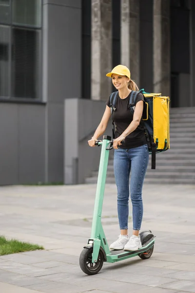 Food delivery female courier rides electric scooter to deliver orders and packages for clients — Fotografia de Stock