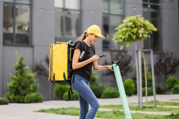 Female courier with thermo backpack browsing address on mobile phone map standing at city street. — Stock Photo, Image