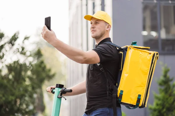 Ο άνθρωπος courier παράδοση τροφίμων με κίτρινο θερμική σακίδιο βόλτες δρόμο με ηλεκτρικά σκούτερ — Φωτογραφία Αρχείου