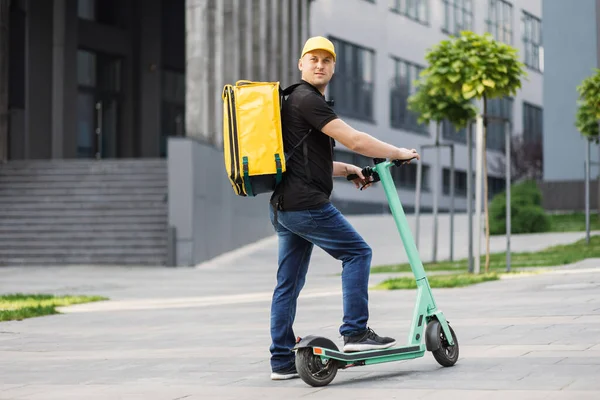 Young happy delivery man riding electric scooter with yellow thermal box backpack — Fotografia de Stock