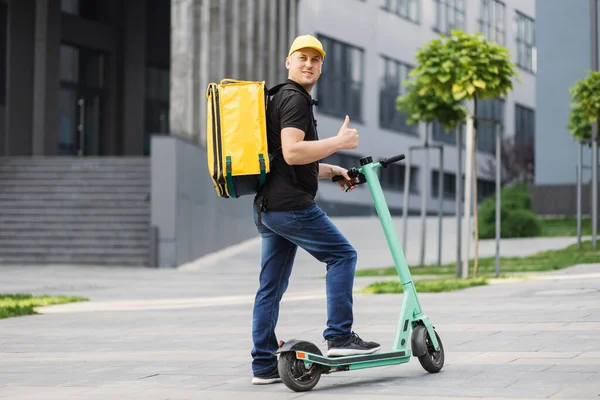 Sarı termal çantalı, elektrikli scooter kullanan mutlu genç teslimatçı.