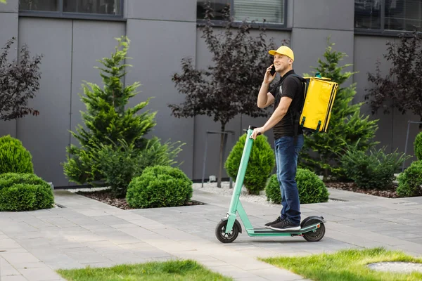 Akıllı telefon kullanan ve şehirde scooter kullanan teslimatçı..