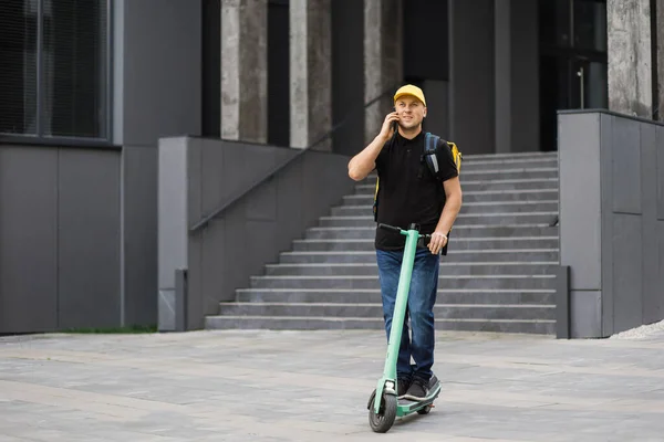 Entrega homem usando smartphone e equitação empurrar scooter na cidade. — Fotografia de Stock