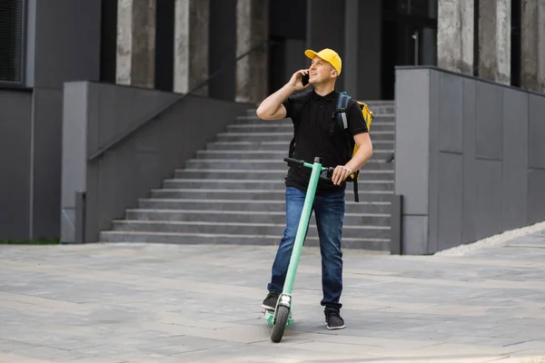 Entrega homem usando smartphone e equitação empurrar scooter na cidade. — Fotografia de Stock