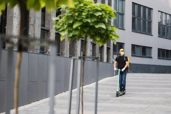 Sarı maskeli bir adam, şehirde sıcak yemek getiren bir scooter kullanıyor.