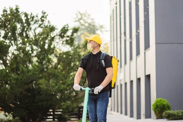 Beyaz tenli teslimatçı, yüz maskeli elektrikli scooter 'la sarı termal çantalı..