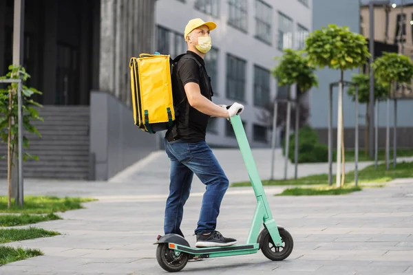 Koerier leveren voedsel op elektrische scooter dragen geel gezicht beschermend masker. — Stockfoto