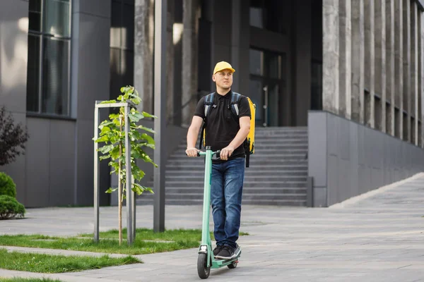 Rijder man levert eten met elektrische scooter in de stad. Ecologisch fast delivery food concept. — Stockfoto