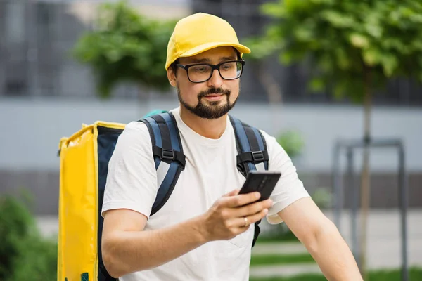 Retrato del repartidor con mochila amarilla y scooter buscando la dirección del cliente en el teléfono — Foto de Stock