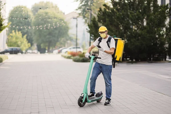 Male courier with isothermal food case box on electric scooter arrives to house and calls for client — Stockfoto
