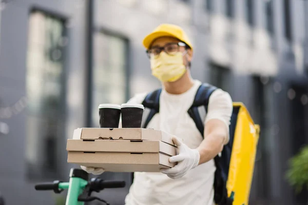 Leverancier in beschermend gezichtsmasker met stapel pizzakartonnen dozen met twee kopjes koffie — Stockfoto