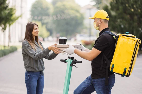 Çekici genç teslimatçı elinde sıcak pizza ve iki fincan sıcak kahve olan kutular tutuyor..