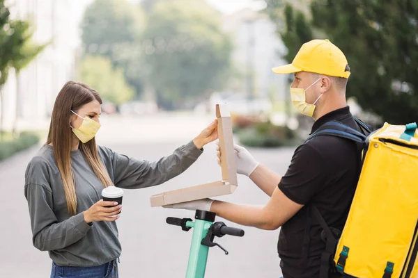 Pizza teslimatı. Sarı üniformalı ve yüz maskeli kurye kadınlara yemek siparişi veriyor..