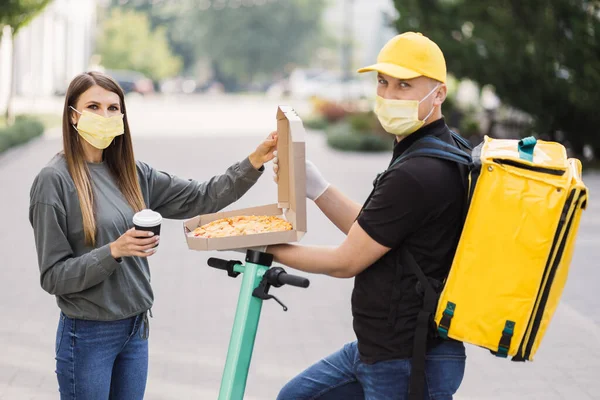 Pizza teslimatı. Sarı üniformalı ve yüz maskeli kurye kadınlara yemek siparişi veriyor..