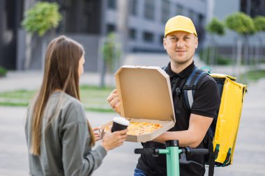 Sarı termal çantalı çekici genç kurye pizza kutusu ve kahve getiriyor.