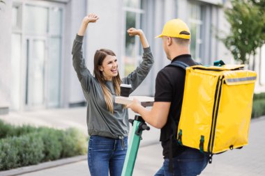 Yemek teslimatı kuryesi elektrikli scooterın üzerinde dururken sipariş veriyor..