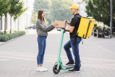 Kafkasyalı çekici kurye, beyaz kız müşterilere karton kutular getiriyor..