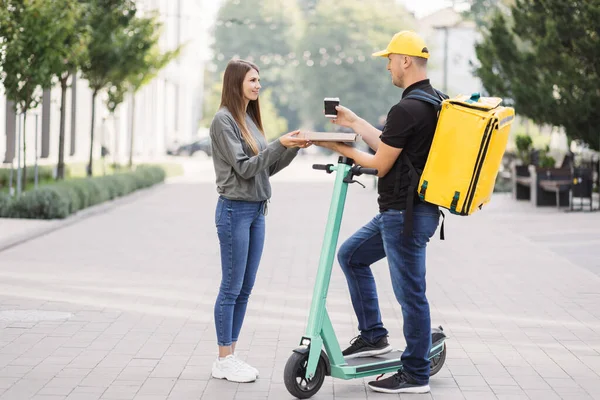 Çekici genç kurye beyaz kız müşteriye pizza kutusu ve kahve getiriyor.