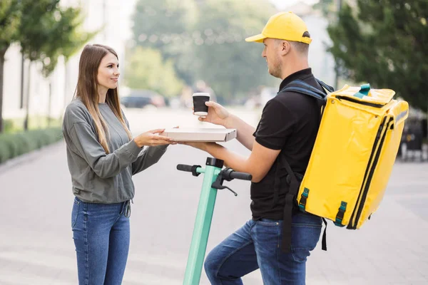 Çekici teslimatçı çocuk elinde sıcak pizza ve sıcak kahve dolu bir kutu tutuyor..