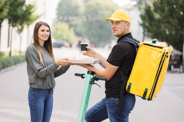 Çekici teslimatçı çocuk elinde sıcak pizza ve sıcak kahve dolu bir kutu tutuyor..