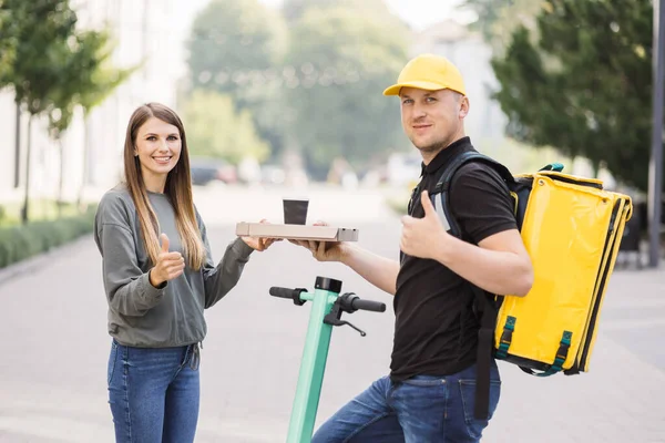 Çekici teslimatçı çocuk elinde sıcak pizza ve sıcak kahve dolu bir kutu tutuyor..