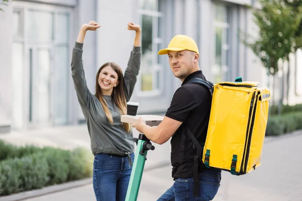 Yemek teslimatı kuryesi elektrikli scooterın üzerinde dururken sipariş veriyor..