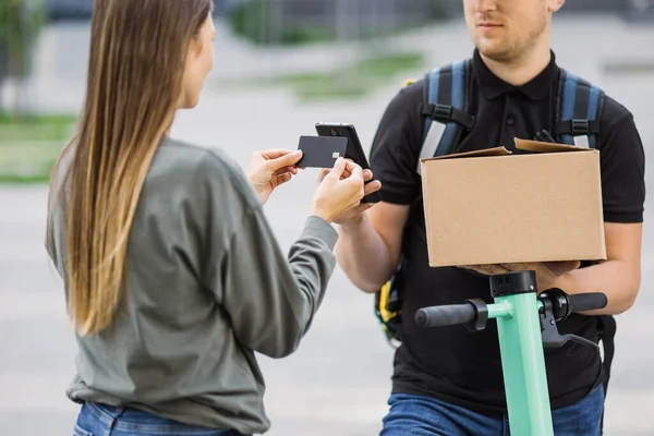 Kafkasyalı genç bir kadın akıllı telefon ve kredi kartıyla para ödüyor.